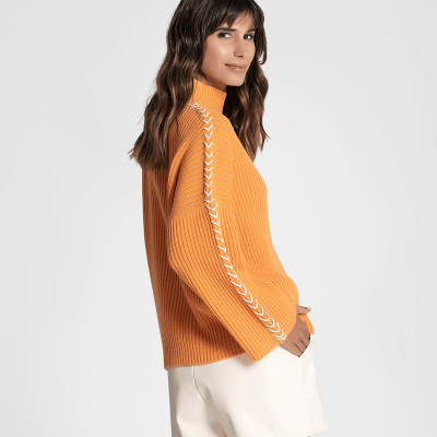 Mulher de perfil a usar camisa de malha laranja com padrão branco nas mangas e calções creme