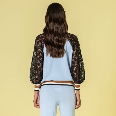 Conjunto de casaco azul claro com mangas de renda preta e calças azuis claras, visto de trás, fundo amarelo.