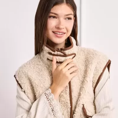 Colete peludo bege com detalhes castanhos e blusa creme com renda nas mangas