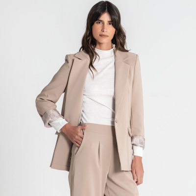 Mulher a vestir blazer bege com padrão geométrico na dobra da manga, calças largas bege e camisola branca de gola alta