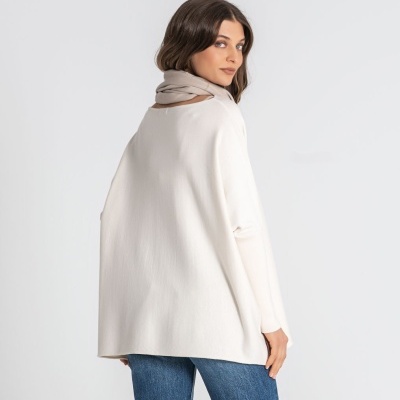 Mulher com camisola branca larga, cachecol bege e jeans azuis de costas