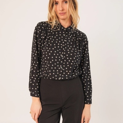 Camisa preta com padrão de bolinhas brancas e calças pretas em modelo feminino