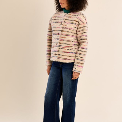Mulher com casaco bege de linhas horizontais coloridas, jeans largos azuis e sapatilhas castanhas.
