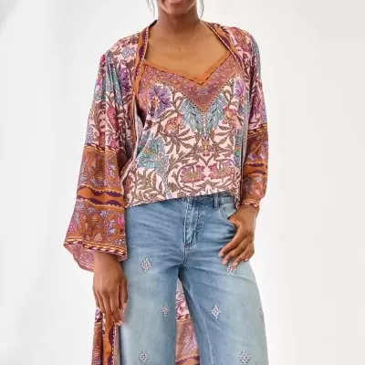 Mulher com blusa floral e casaco comprido rosa e laranja, calças jeans bordadas