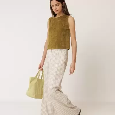 Mulher vestindo top verde-oliva, calças xadrez beige e branco, sandálias castanhas e a carregar bolsa amarelo claro.