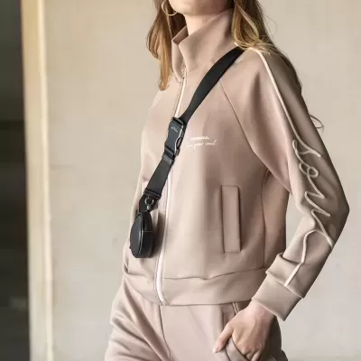 Mulher com conjunto desportivo bege, boné bege e bolsa preta azul