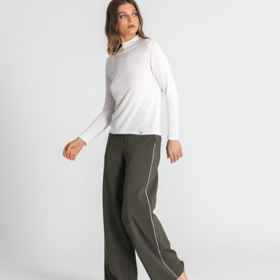 Mulher com camisola branca, calças largas verde-escuro com risca branca e sapatos bege, fundo branco.