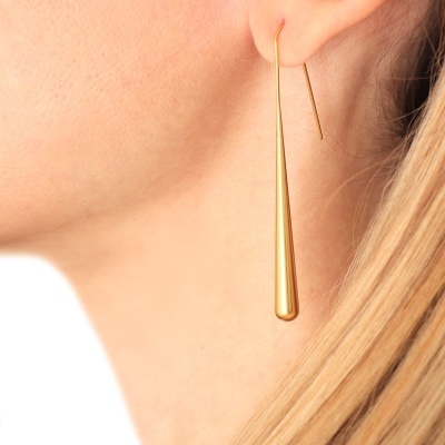 Brinco dourado longo em forma de gota na orelha de pessoa com cabelo loiro