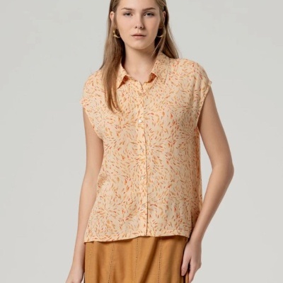 Blusa feminina creme com padrão abstrato e botões frontais, usada com saia castanha em fundo cinza neutro
