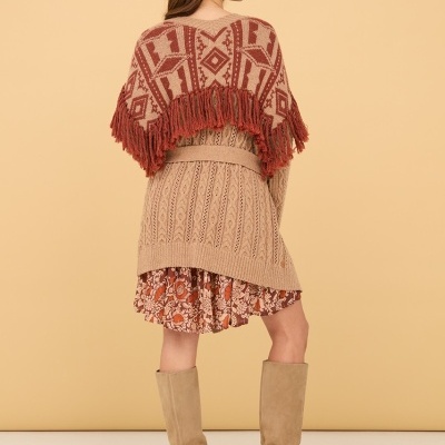 Mulher com vestido floral, cardigan, poncho com franjas e botas bege, vista de costas