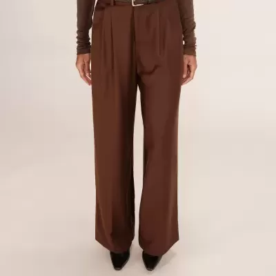 Calças castanhas largas com cinto castanho e camisa castanha, sapatos pretos