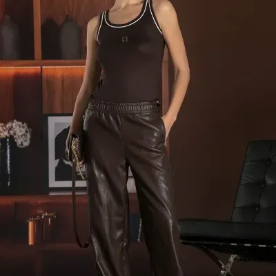 Mulher com roupa castanha e branca, boné castanho, com carteira e sapatos brancos