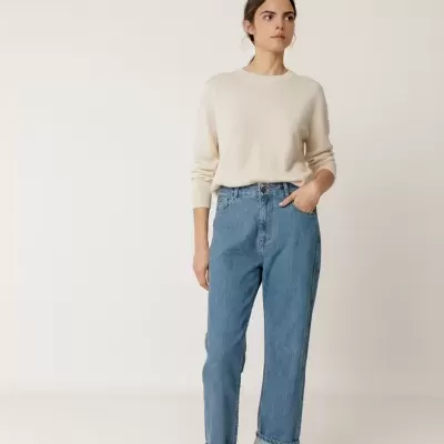 Modelo com camisola bege, jeans azul e ténis cinza em fundo branco