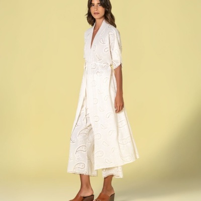 Conjunto branco feminino com vestido longo bordado e calças largas, calçado de cunha castanho.