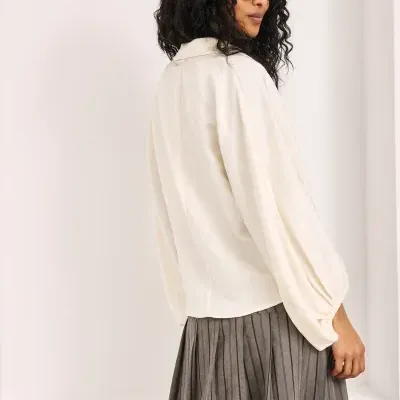 Mulher com blusa creme e saia cinza plissada, usando óculos escuros, em fundo branco