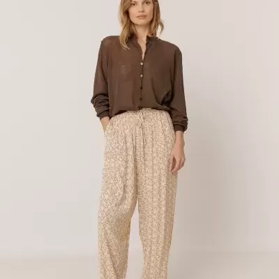 Modelo com camisa castanha, calças creme com padrão floral e sandálias castanhas