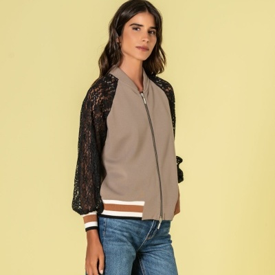 Casaco bege com mangas de renda preta e fecho, combinado com jeans azul