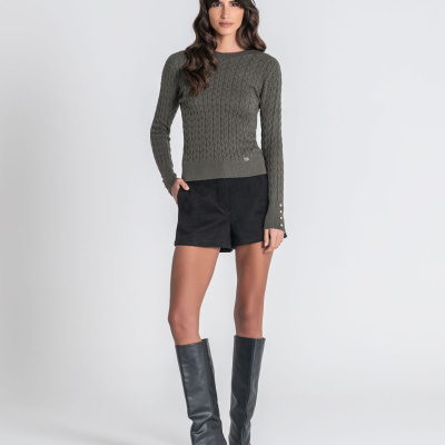 Mulher com camisola de malha verde, calções pretos e botas pretas de salto alto.