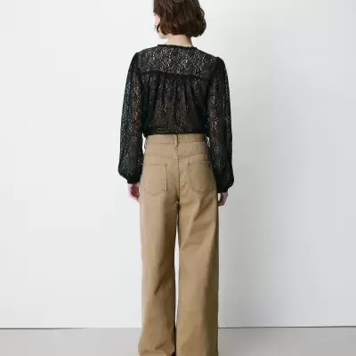 Pessoa de costas com blusa preta de renda e calças bege largas