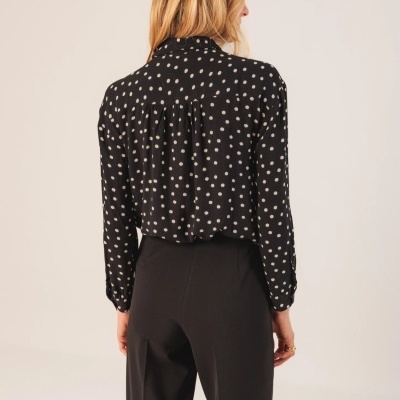 Camisa preta de bolinhas brancas vista de costas com calças pretas.