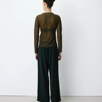 Pessoa de costas com camiseta semi-transparente castanha e calças largas pretas
