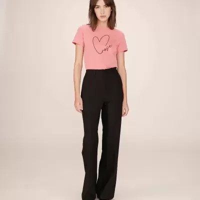 Mulher com t-shirt rosa com coração e calças pretas a fundo neutro
