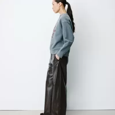 Mulher de perfil a usar sweatshirt cinzenta e calças castanhas largas com padrão enrugado