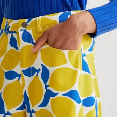 Calças estampadas com limões amarelos e folhas azuis, com bolso e botão metálico, usada com camisola azul canelada