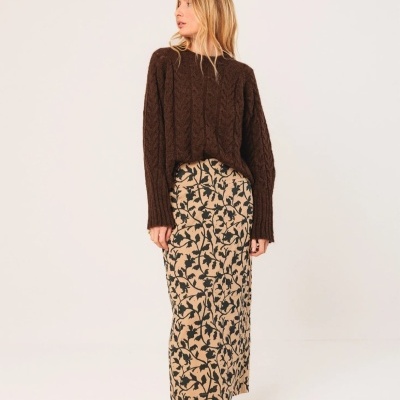 Mulher com camisola castanha de malha, saia comprida creme com padrão floral castanho escuro, e sapatos castanhos com padrão animal print