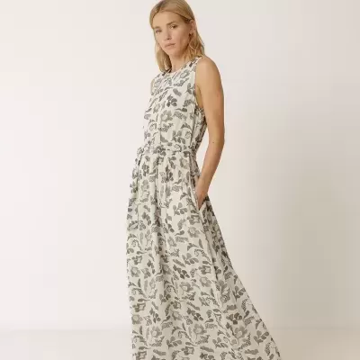 Mulher com vestido longo floral e sandálias castanhas em fundo branco.