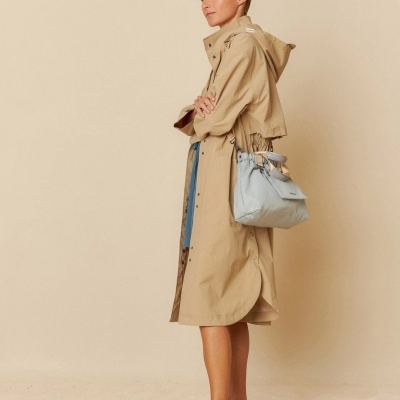 Mulher de perfil com casaco impermeável bege e mala azul clara