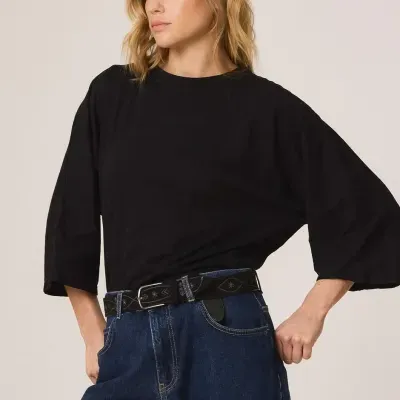 Mulher de cabelo loiro a usar t-shirt preta de manga 3/4 e jeans azul com cinto preto decorado