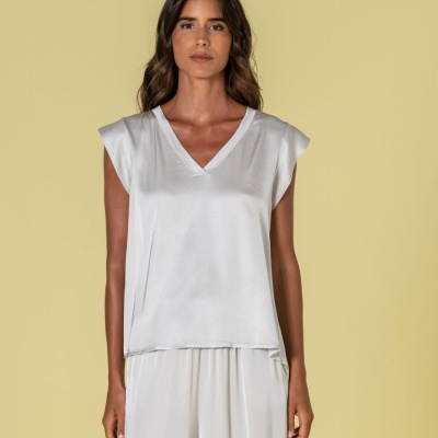 Mulher a usar camisa branca acetinada de decote em V com calças brancas largas