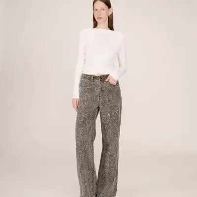 Pessoa com camisola branca de manga comprida e calças largas cinza com padrão abstrato