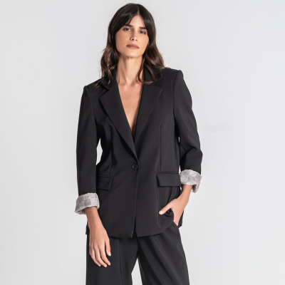 Conjunto de fato feminino preto com blazer de um botão e calças largas, mangas do blazer dobradas mostrando forro cinzento com padrão.