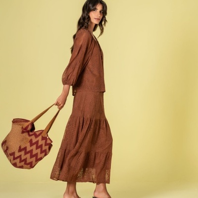 Mulher com roupa castanha rendada e mala de palha com padrão vermelho