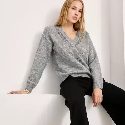 Mulher com camisola cinza e calças pretas sentada num fundo branco