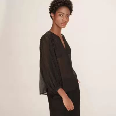 Blusa preta semitransparente com mangas bufantes e calças pretas, modelo de perfil em fundo claro