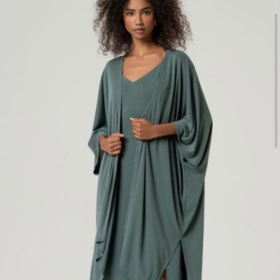 Mulher vestindo uma veste e vestido verde-acinzentado fluido sobre fundo cinzento