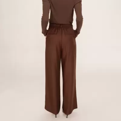 Pessoa de costas com camisola castanha de manga comprida e calças castanhas largas.