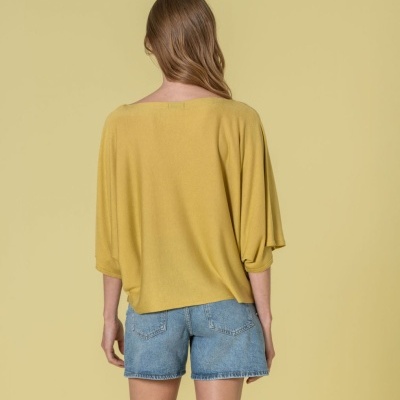 Mulher de costas com blusa amarela e calções de ganga em fundo amarelo