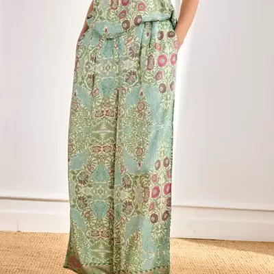 Calças largas com padrão floral verde, azul e rosa e sandálias douradas