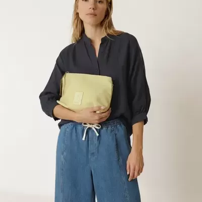 Mulher com camisa preta, calças largas de ganga azul e bolsa bege com etiqueta quadrada