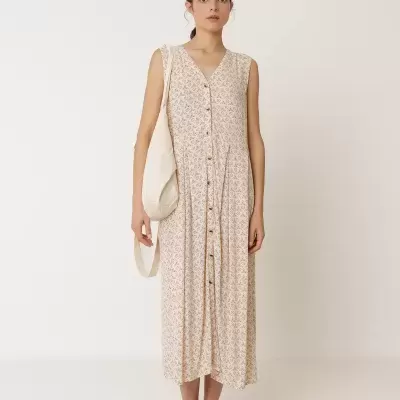 Vestido comprido de mulher com padrão floral bege, botões frontais, mala branca e sandálias castanhas