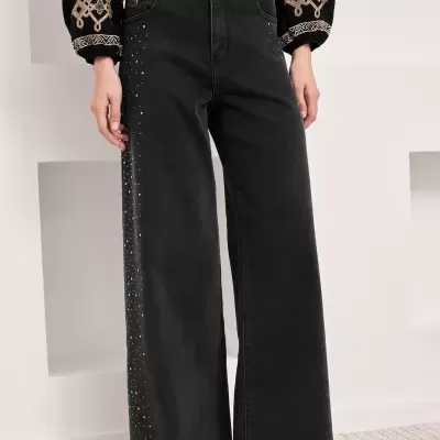 Calças de ganga pretas largas com detalhes de pedras brilhantes e camisa bordada.