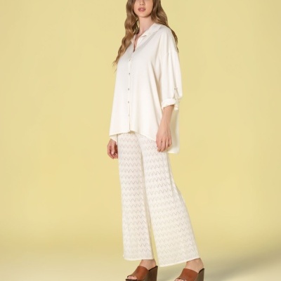 Modelo feminina com blusa branca, calças brancas com padrão em zig-zag e plataformas castanhas, em fundo amarelo.