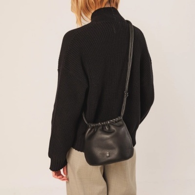 Mulher de costas com camisola preta e calças bege transporta mala preta ao ombro