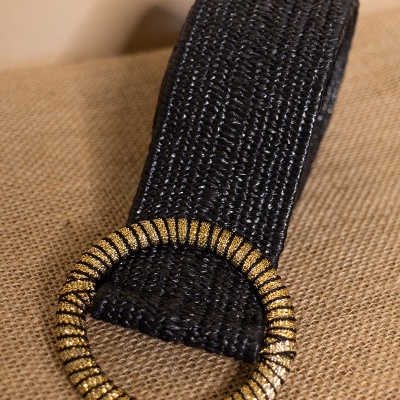 Cinto preto com fivela redonda dourada sobre tecido castanho claro