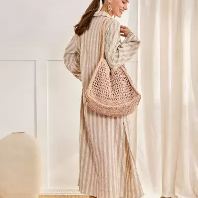Mulher com vestido riscado e mala de crochê num ambiente interior claro