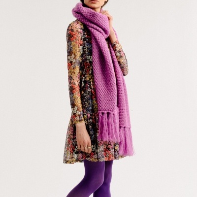 Mulher com vestido floral colorido, collants roxos, botas pretas e cachecol roxo grande